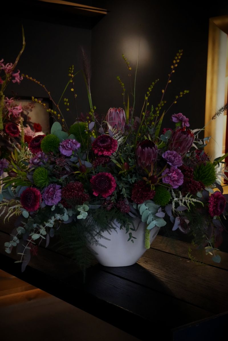 Üppiges Gesteck mit dunkelroten Dahlien, violetten Nelken, grünen Chrysanthemen und Eukalyptus in einer Schale