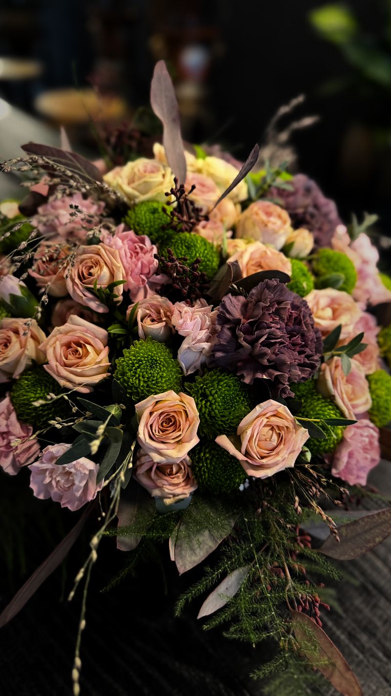 Nahaufnahme eines Gestecks aus apricotfarbenen Rosen, zartrosa Nelken und hellgrünen Chrysanthemen