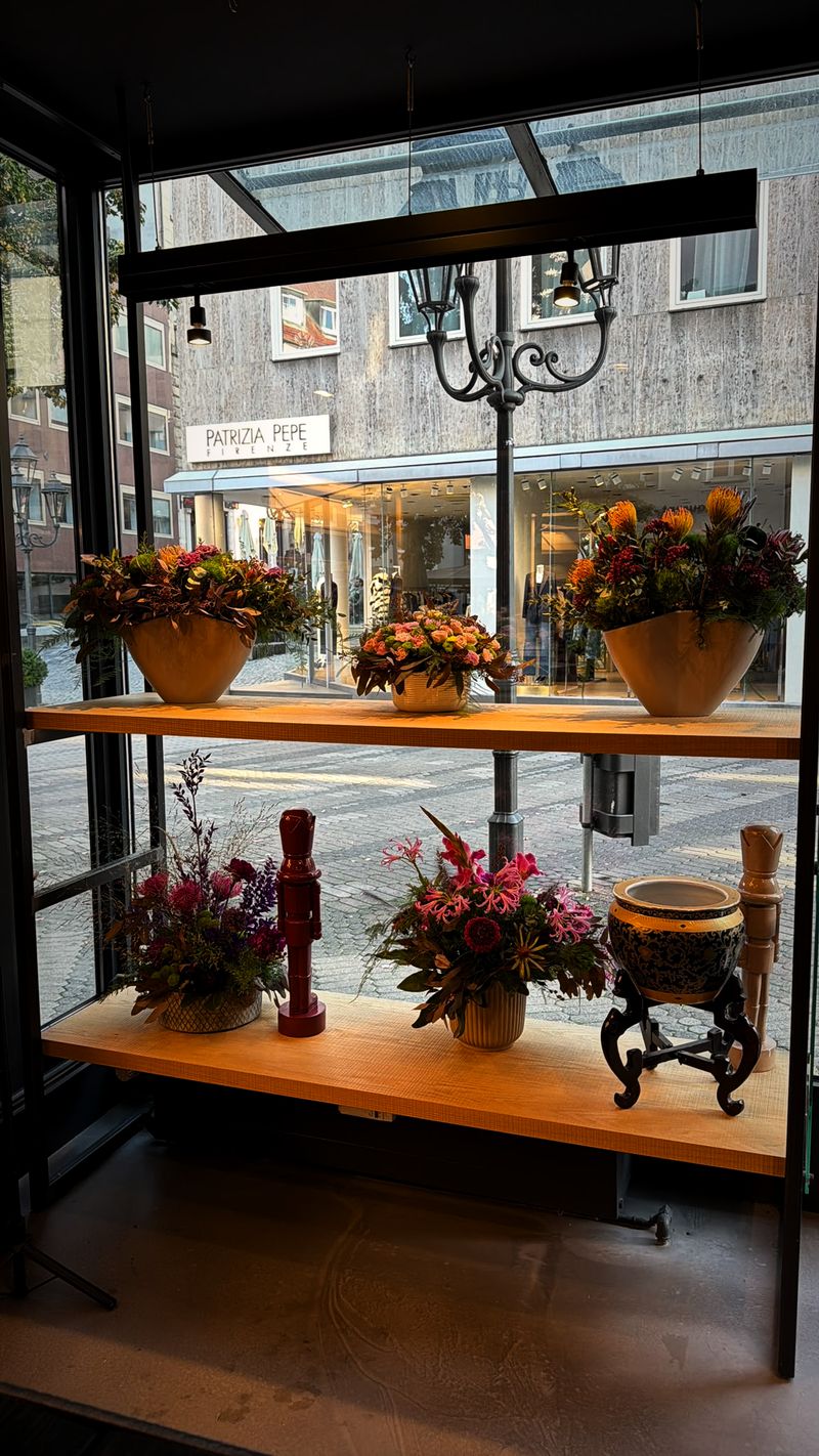 Schaufenster von Blumenkind mit Gestecken auf hellen Holzregalen, dahinter die Kaiserstraße in Nürnberg