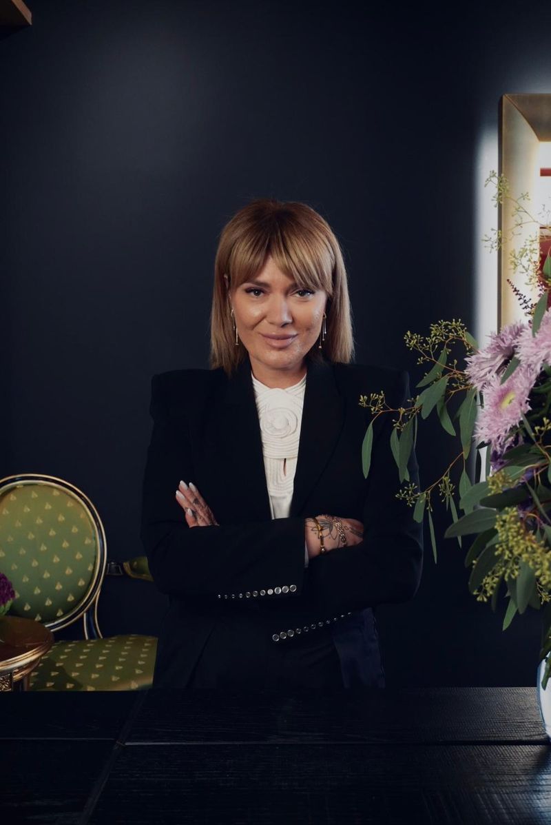 Elmira Kinderknecht, Gründerin von Blumenkind, im schwarzen Blazer in ihrer Blumengalerie, neben ihr ein Strauß in Rosa und Grün