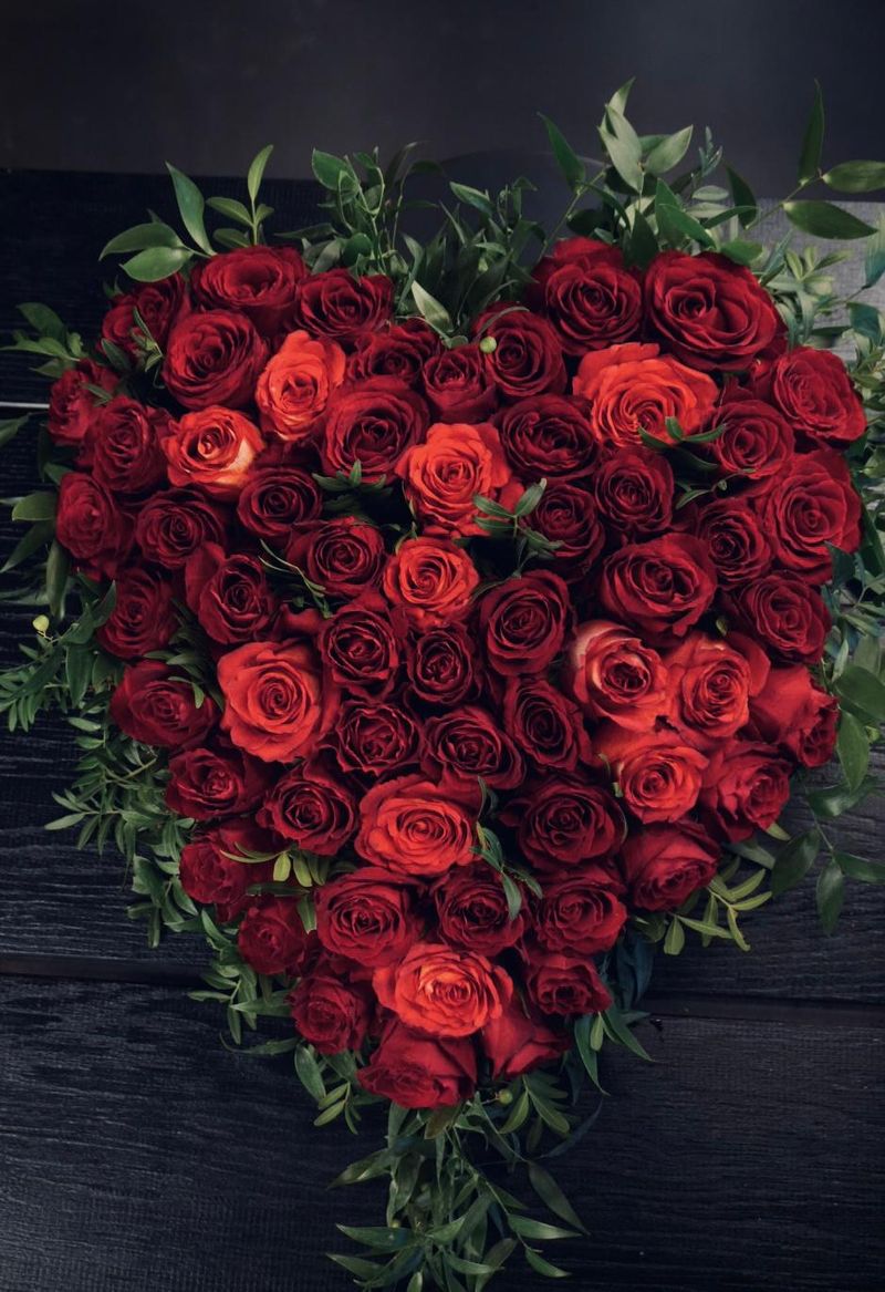 Großes Herz aus roten und orangeroten Rosen mit frischem Grün auf einem dunklen Holztisch