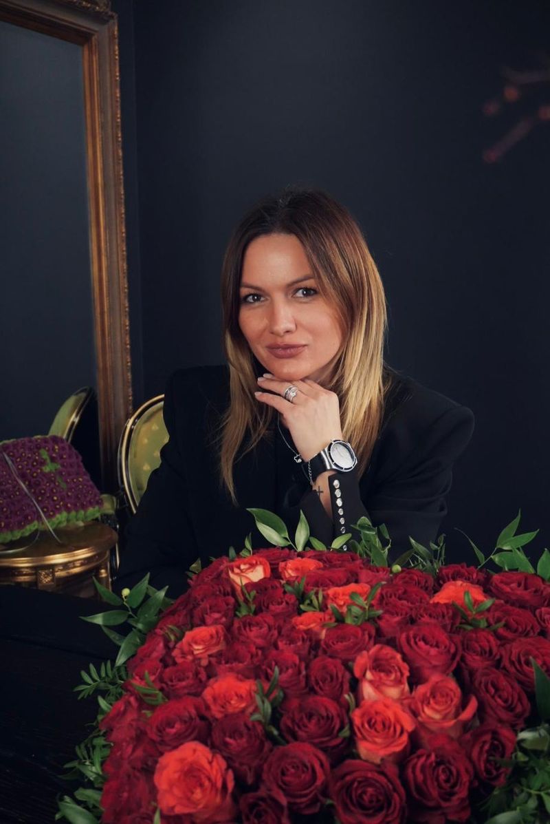Margarita, erfahrene Floristin bei Blumenkind, im schwarzen Blazer hinter einem großen Herz aus roten Rosen